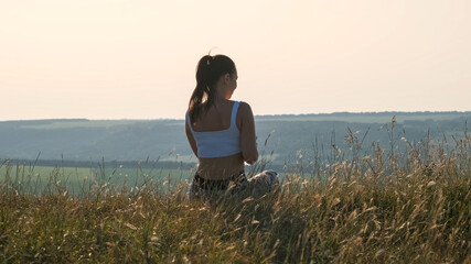 The young sportive woman sitting at the mountain top