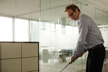Fototapeta na wymiar Businessman putting golf ball in office