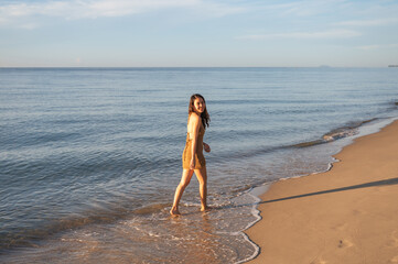 Young asian woman in brown dress walking on the beach in the morning at tropical sea on vacation