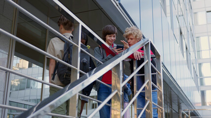 Low angle view of multiethnic teen students with cellphone talk near stairs outside school