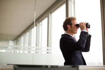 Businessman using binoculars at office window