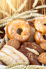 Various types of bread and  other pastries in wicker tray on lace tablecloth with wheat ears in wheat field background  