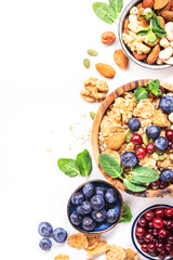 Muesli bowl and organic ingredients for healthy breakfast. Granola, nuts, blueberry, cranberry, oatmeal, greek yoghurt, whole grain flakes on white table