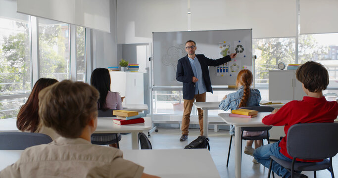Back view of multiethnic teen students in classroom listen to teacher and raise hand to answer question