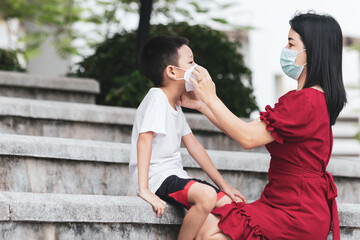 Mom is wearing a medical mask for her child. Little asian boy and mom in medical mask. Asian family protection virus concept.