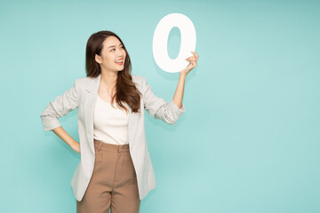 Young beautiful Asian businesswoman showing number 0 or zero isolated on green background - obrazy, fototapety, plakaty