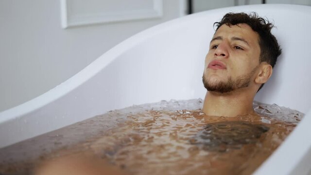 Man sits with closed eyes in the bath with ice cubes for recovery