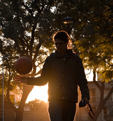 Chico con rastas jugando al baloncesto en un parque durante el atardecer