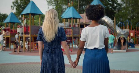 Rear view of diverse lesbian couple holding hands standing on outdoors playground