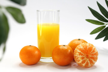 tangerine juice in a glass and tangerines on a white plate with tropical leaves