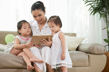 Young mother and her two little daughters watching animated cartoon on tablet computer at home