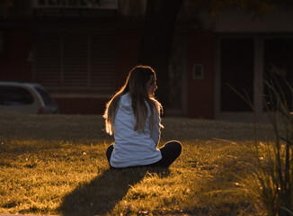 Mujer sentada sobre el pasto de espaldas bajo los rayos del sol