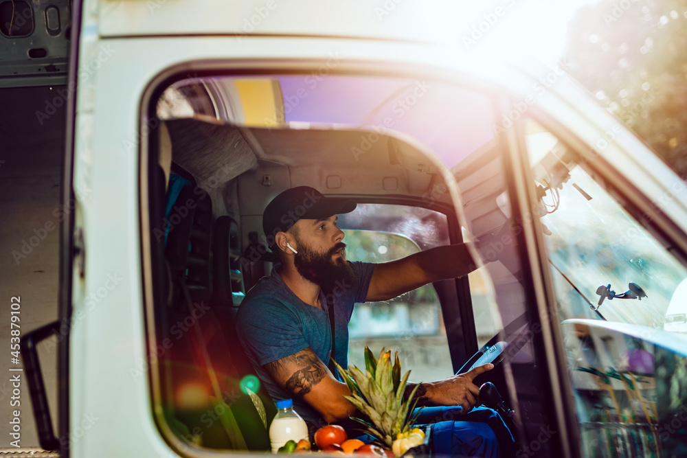 Wall mural young bearded man is driving delivery van. he is working in everyday or daily home delivery service.