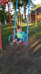 child playing on playground. Little boy swinging on a swing. Children's swing in the park. Playground for children. - 453881785