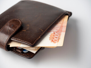 A close-up of a leather wallet full of 5000 rubles banknotes lies on a white background. Side view