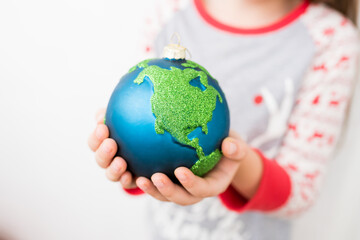 Merry christmas and new year concept. Close-up of little girl holding in hands Xmas glass bauble decoration ornament globe planet earth. Selective focus