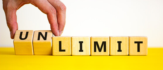 Limit or unlimit symbol. Businessman turns cubes, changes words 'limit' to 'unlimit'. Beautiful yellow table, white background, copy space. Business, limit or unlimit concept.