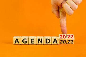 Planning 2022 agenda new year symbol. Businessman turns wooden cubes and changes words 'Agenda 2021' to 'Agenda 2022'. Beautiful orange background, copy space. Business, 2022 agenda new year concept.