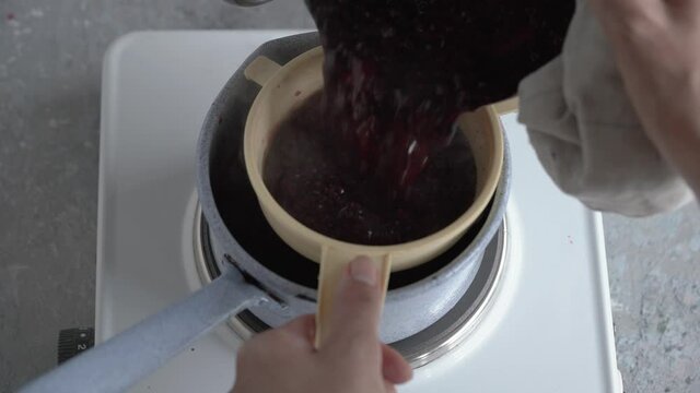 Preparation of homemade black elder syrup - draining and separting the beverage from the cooked crushed elderberries and spices