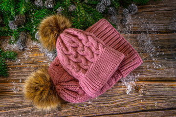 Warm knitted pink hats with pompom for mother and daughter. Christmas decoration on wooden background, flat lay. 