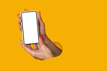 Woman holding in hand smartphone with blank screen isolated on yellow background. Creative technology concept.