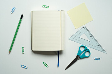 notebook with space for text, desk, reminder, yellow card, blue bookmark, green pencil, ruler, scissors, paper clips, on a white background, photo from above