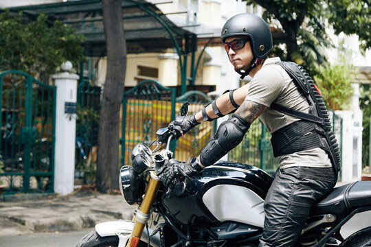 Serious handsome young man in protective gear sitting on motorcycle resy to ride