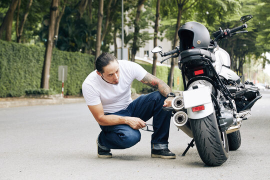 Handsome fit man checking his motorcycle broke on road after long ride