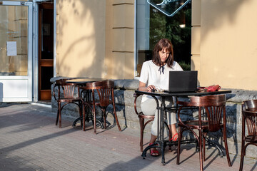 A young woman is sitting at a laptop in a summer street cafe. people using social media