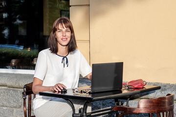 A young woman is sitting at a laptop in a summer street cafe. people using social media