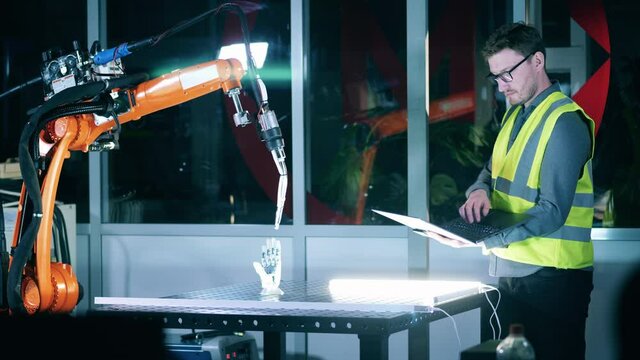 Male engineer in safety wear is studying a robotic mechanism