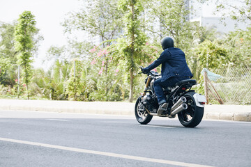 Man in jeans and denim jacket riding on motorcycle on highway, view from the back