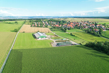 Aerial shot of a cow farmer business with a beautiful vilylage next to it, surrounded by nature.