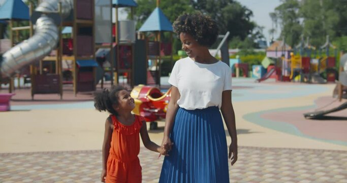 Slider shot of afro mother and daughter holding hands walk at playground