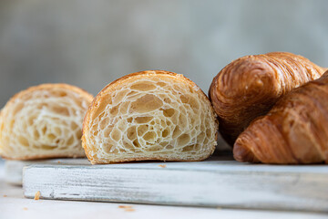 Cut in half croissant with inside texture and thin crisp layers on wooden board, light concrete background. Delicious french pastry.