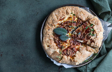 Savory tomato tart, open pie or galette with tomatoes and cheese decorated with aromatic herbs on green background. Top view.