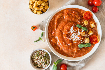 Vegetable soup with baked tomato, bell pepper, cream, breadcrumbs and micro greens in white bowl on light concrete background. Top view.