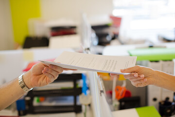 Businesswoman passing folder to colleague over desk