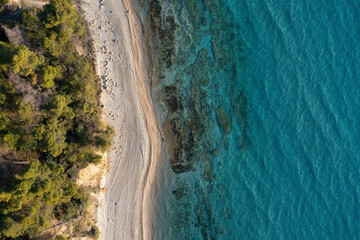 Aerial top down view to a narrow sand beach stripe bounded by a green forest and turquoise sea