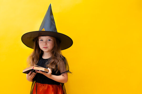 An emotional portrait of a cheerful kid girl in a witch costume on a yellow colored background. Halloween. A place for text.