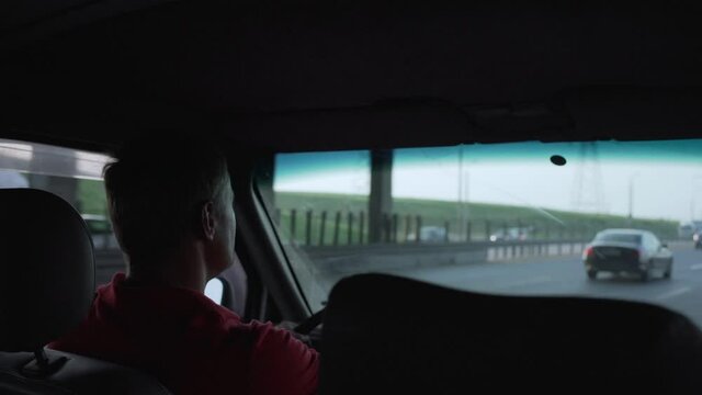 concentrated tired man with gray hair in red T-shirt rides minivan home on turn and spins steering wheel and drives off highway