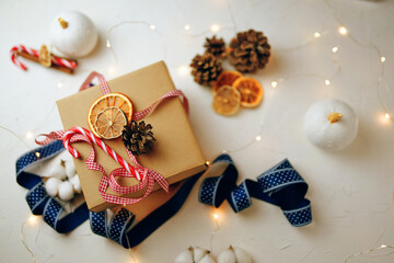 Top view of christmas gift box and decorations on white textured table. Candy cane, colorful ribbons, garlands, dried orange slices and cones. New Year's atmosphere. Wintertime. Festive still life.