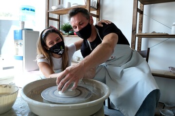 A young couple in black medical masks "covid-19 firewall" work with white clay on a potter's wheel. The concept of privacy and creativity. pottery wheel.