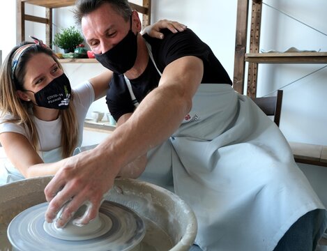 A young couple in black medical masks "covid-19 firewall" work with white clay on a potter's wheel. The concept of privacy and creativity. pottery wheel. 