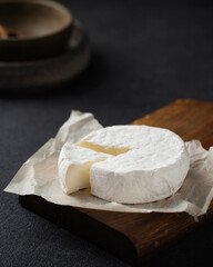 Fototapeta na wymiar Brie cheese on a wooden board. A piece of camembert. French cuisine. An aperitif on a dark background.
