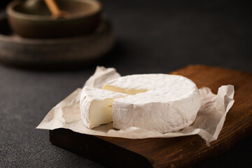 Brie cheese on a wooden board. A piece of camembert. French cuisine. An aperitif on a dark background.