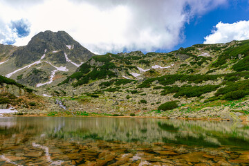 Glacial lake in the mountains landscape in summer. Lovely landscape photography of a mountain lake with mountain peaks in the background. Weather is sunny with a couple pf clouds. 