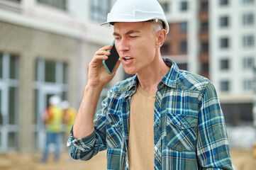 Gray-haired male builder talking on his cellphone outdoors