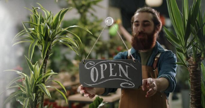 Flower shop employee flipping sign on glass entrance door from open to closed, finishing workday of greenhouse. Small business people 4k footage