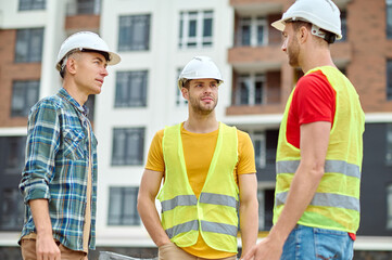 Three builders in protective helmets having a conversation outdoors